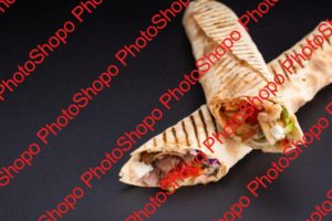 Shawarma sandwich - fresh roll of thin lavash or pita bread filled with grilled meat, mushrooms, cheese, cabbage, carrots, sauce, green. Traditional Eastern snack. On black background.